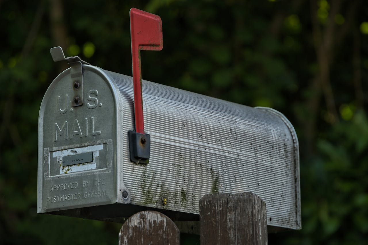 A classic U.S. mailbox with a red flag in a green outdoor setting, evoking nostalgia.